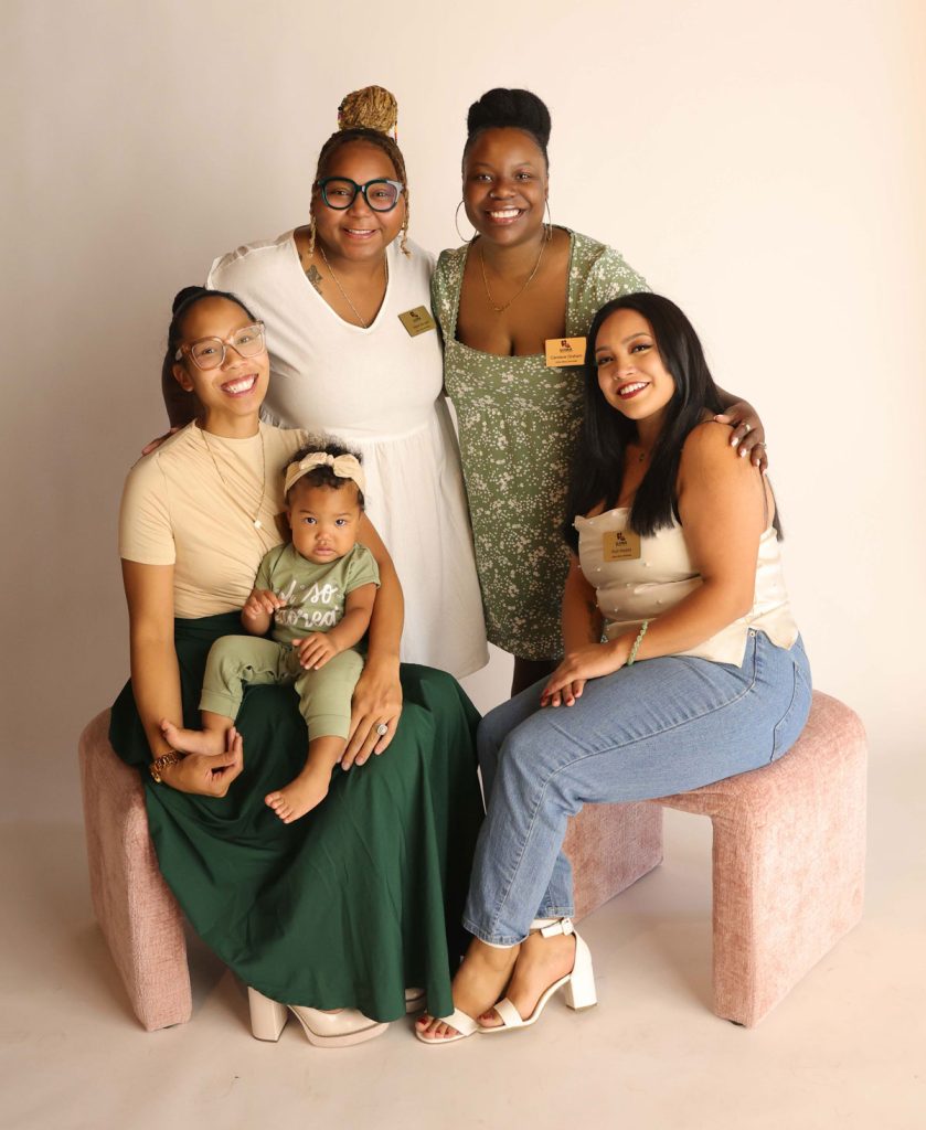 Ujima Maternity Network - Mom Advocates MCCO- Sista Circle. Image of a group of women smiling, one holding a baby.